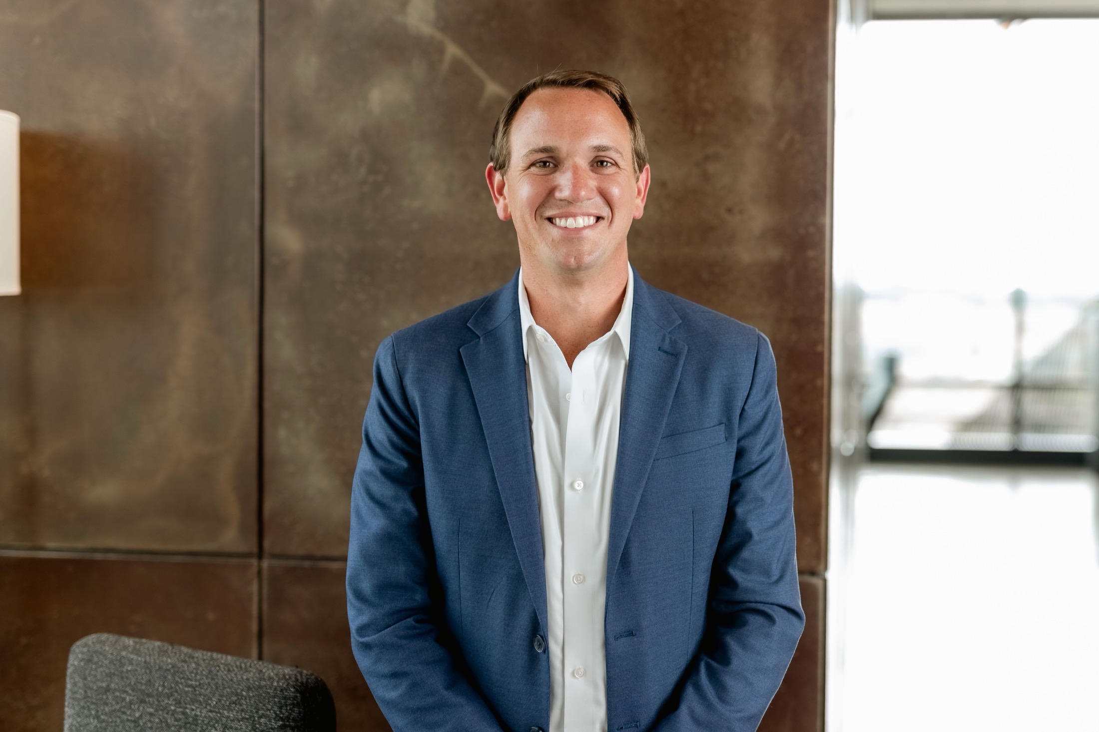 Brian Onorio smiling in a navy blazer in front of a weathered steel wall